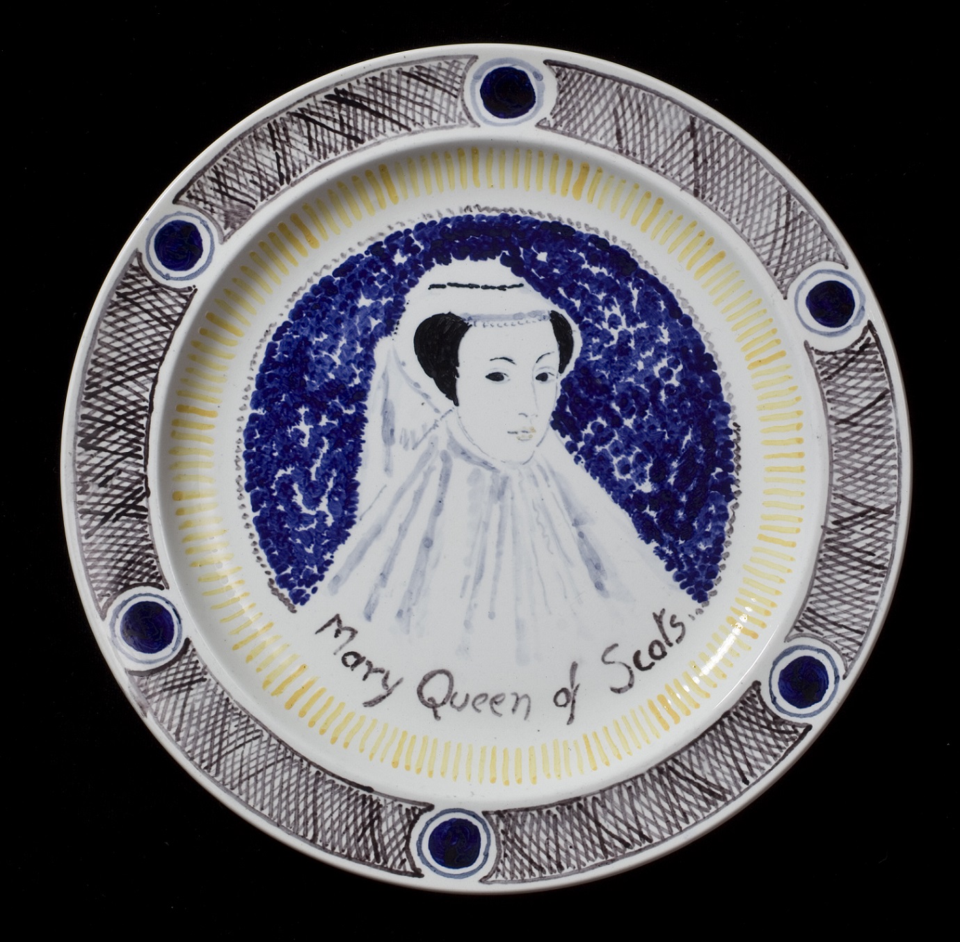 A photograph of a plate from 'The Famous Women Dinner Service'. The portrait is a bust of Mary Queen of Scots in a headress and flowing white garment. The background is dark blue, and the rim is decorated with a repeating pattern.